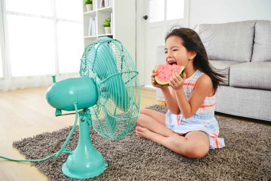 Girl eating watermelon in front of a fan before a new AC is installed.