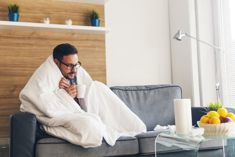 Man on the couch wrapped in a blanket.