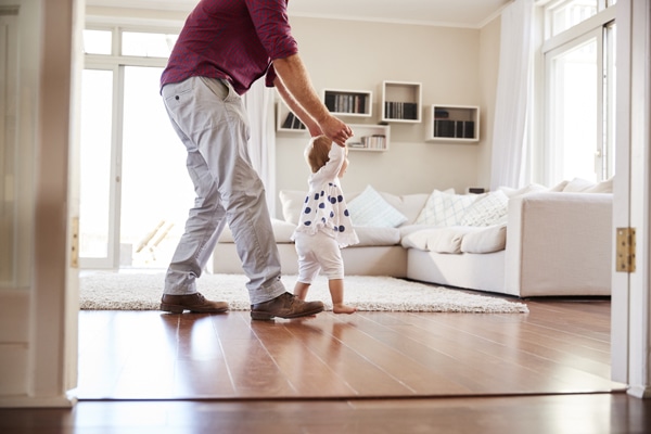 Father helping daughter learn to walk at home.