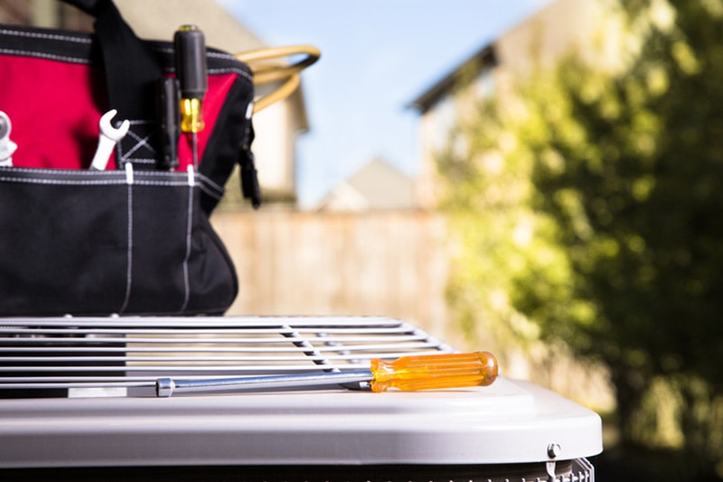 Bag of repairman's work tools, screwdriver on top of air conditioner unit outside brick home, Common AC Problems and Solutions | HVAC Maintenance | La Porte, TX