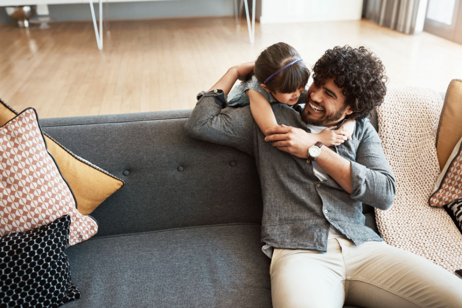 Dad on couch with daughter hugging him.