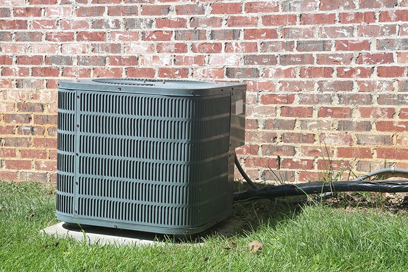 Home Air Conditioner Condenser coil sitting in front of brick wall, Top Causes of AC Failure | HVAC Maintenance, Repair | Pasadena, TX