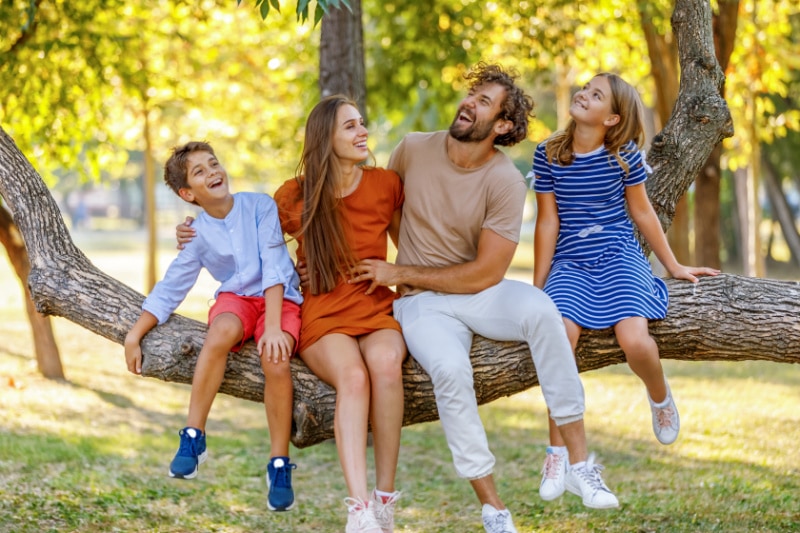 Family in backyard laughing while they sit on large tree branch, waiting for La Porte HVAC contractors.